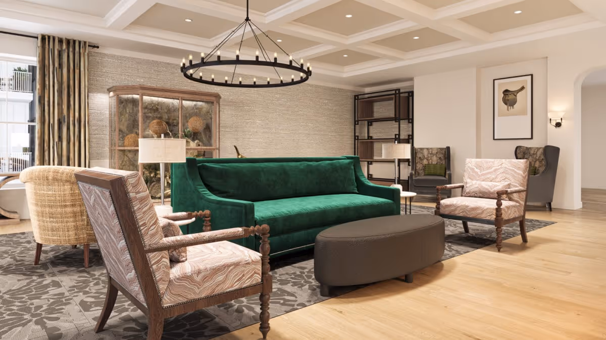 A spacious and elegantly furnished living room with a green velvet sofa, two patterned armchairs, a beige armchair, a dark oval ottoman, and a large patterned rug. The room features a coffered ceiling with a circular chandelier, wooden flooring, a glass cabinet with decorative items, and a framed bird artwork on the wall.