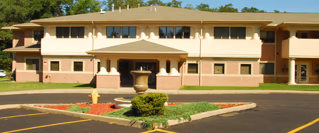 Front exterior of a two-story senior living building with a fountain, circular driveway, and landscaped island.