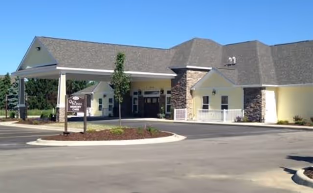 Single-story yellow retirement facility entrance with a covered porte-cochere, circular driveway, and a small sign in front.