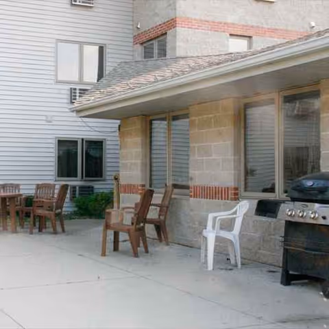 Outdoor patio area with plastic chairs, a table, and a grill beside the building.