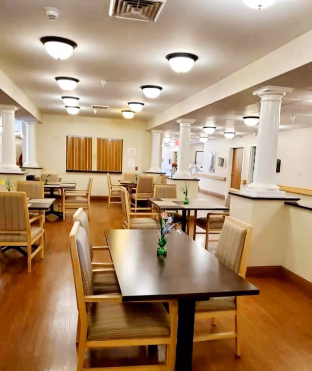 Bright communal dining room with multiple tables and chairs, decorative white columns, and ceiling lights.