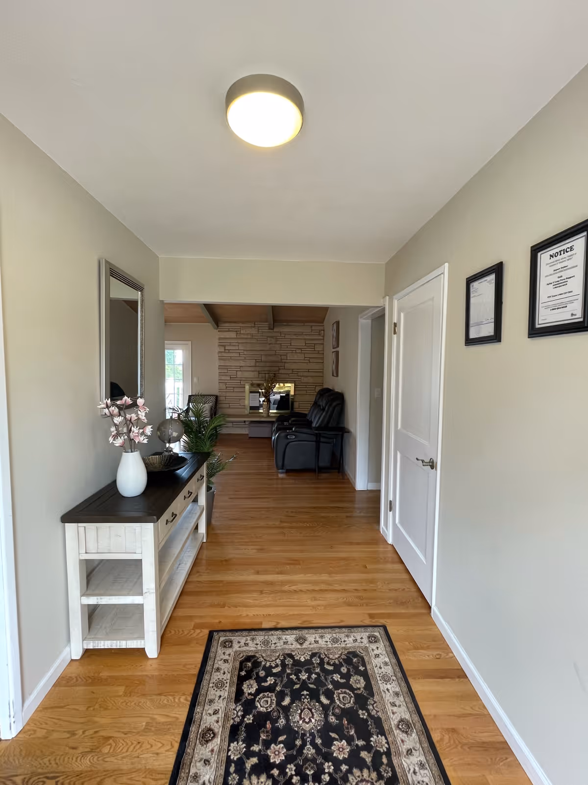 Entry hallway with wooden floors, a console table and rug leading into a living room with recliners and a fireplace.