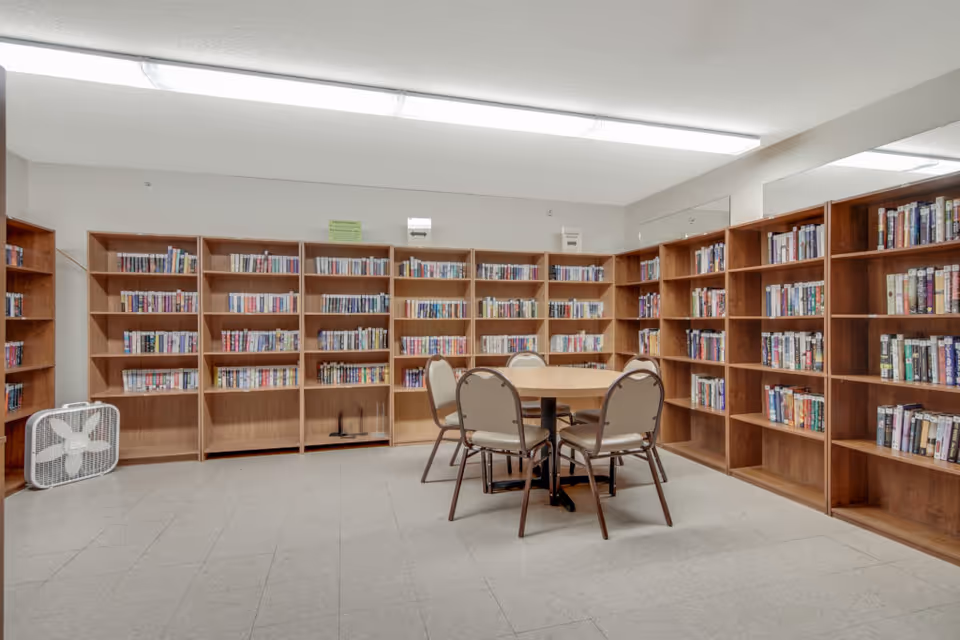 Interior room with wooden bookshelves lining the walls and a round table with four chairs in the center.