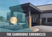 Exterior view of Cambridge Senior Living facility showing the entrance with a covered drop-off area, brick and beige walls, and clear blue sky.
