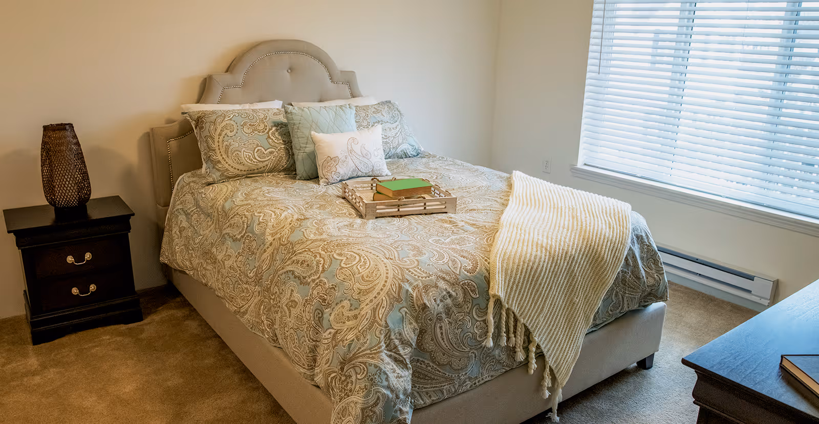 Neat bedroom with a patterned bed, decorative pillows and throw, nightstands, and a window with blinds.