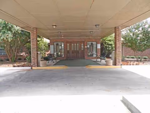 Covered drop-off area with brick columns leading to double doors of a facility entrance.