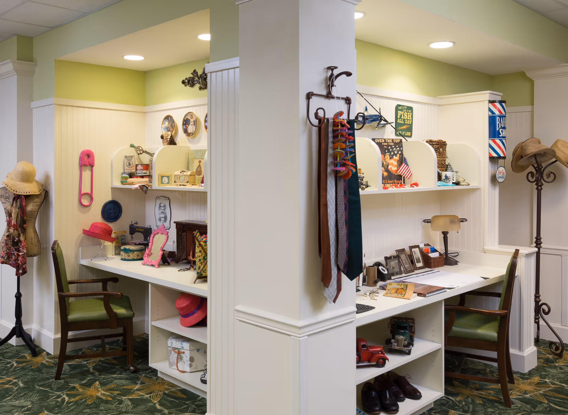 Two small workstations with green chairs in a cozy corner area decorated with vintage items, hats on stands, ties hanging on a wall hook, and various decorative objects on shelves and desks. The walls are light green and white with recessed lighting overhead.