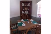 Small dining area with a wooden table set for four and a corner hutch displaying plates.
