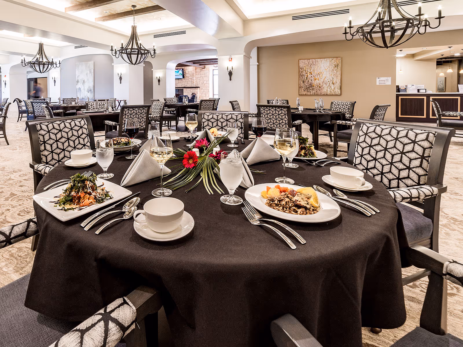 Spacious dining room with a round table set with plates, wine glasses, napkins, and a floral centerpiece.