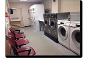 Laundry room with multiple washers and dryers along one wall and a row of chairs along the opposite wall.