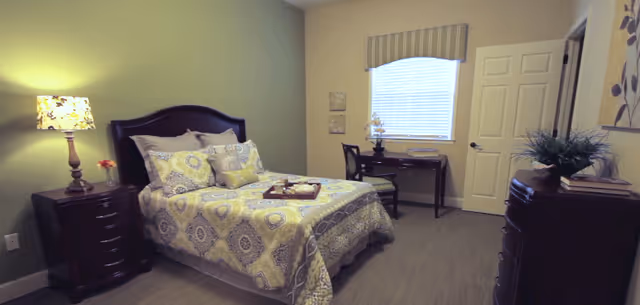 Furnished bedroom with a patterned bed, nightstands and lamp, a desk by the window, and a dresser.