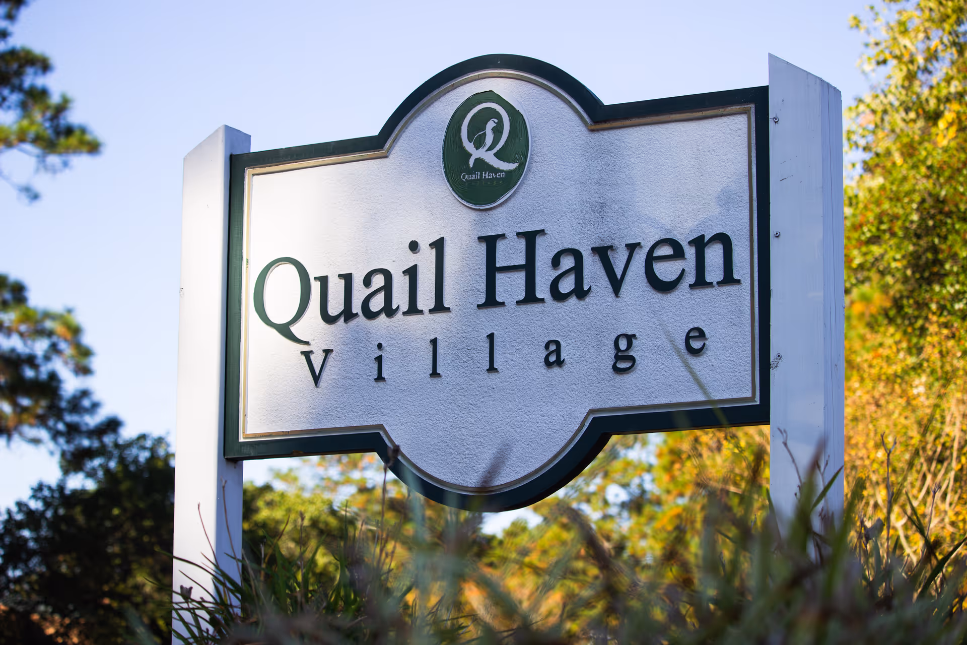 Outdoor sign reading "Quail Haven Village" set among trees and landscaping.