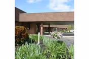 Covered brick building entrance with a porte-cochere, landscaped shrubs in front, and a driveway.