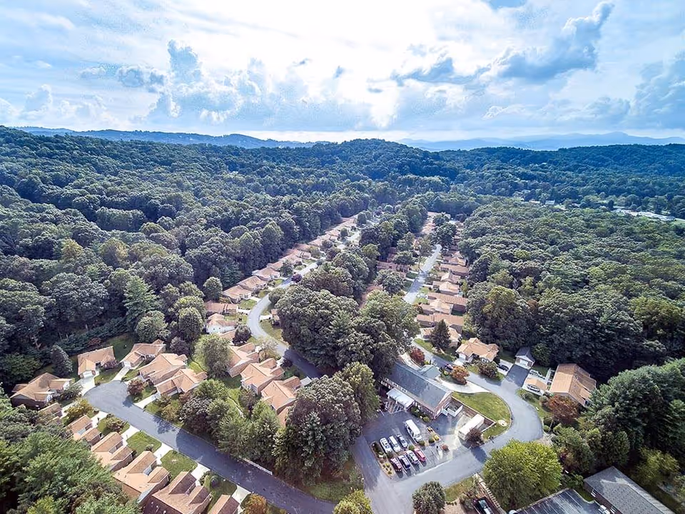 Aerial view of a senior living community with rows of single-story homes surrounded by dense trees and winding roads.