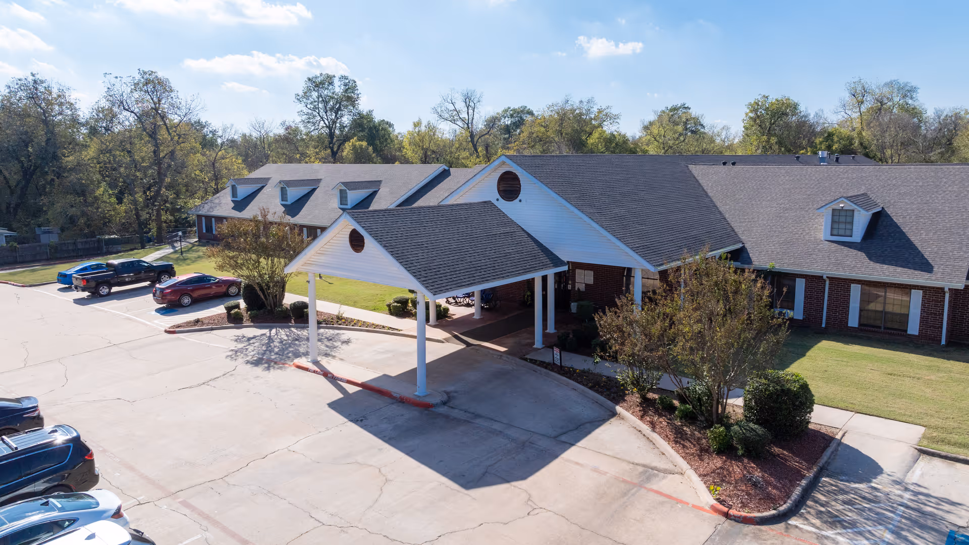 Front entrance with a covered porte-cochere of a single-story senior care building, adjacent parking lot, and landscaping.