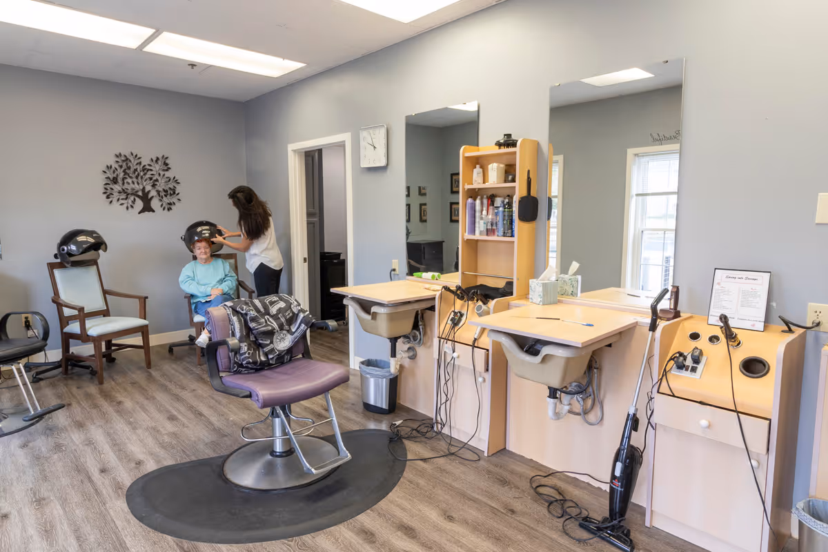 Interior salon area with styling chairs, sinks and a stylist attending to a seated resident.