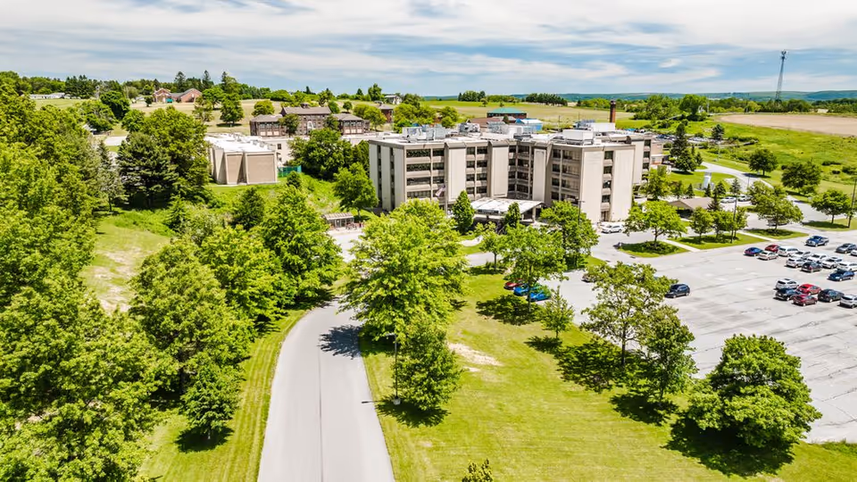 Aerial view of a senior living campus with a central building, trees, and parking.