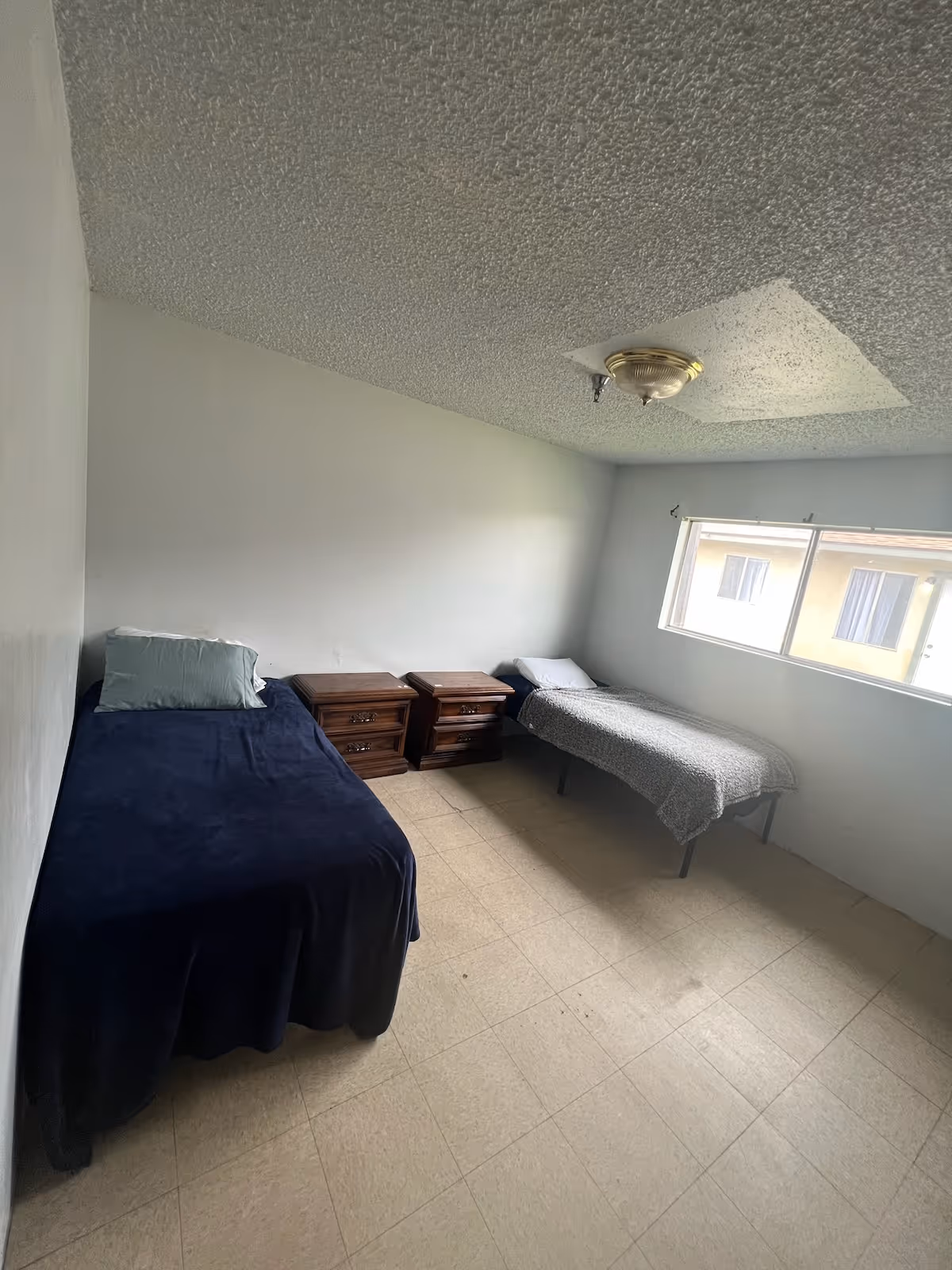 Two single beds and nightstands in a small, sparsely furnished bedroom.