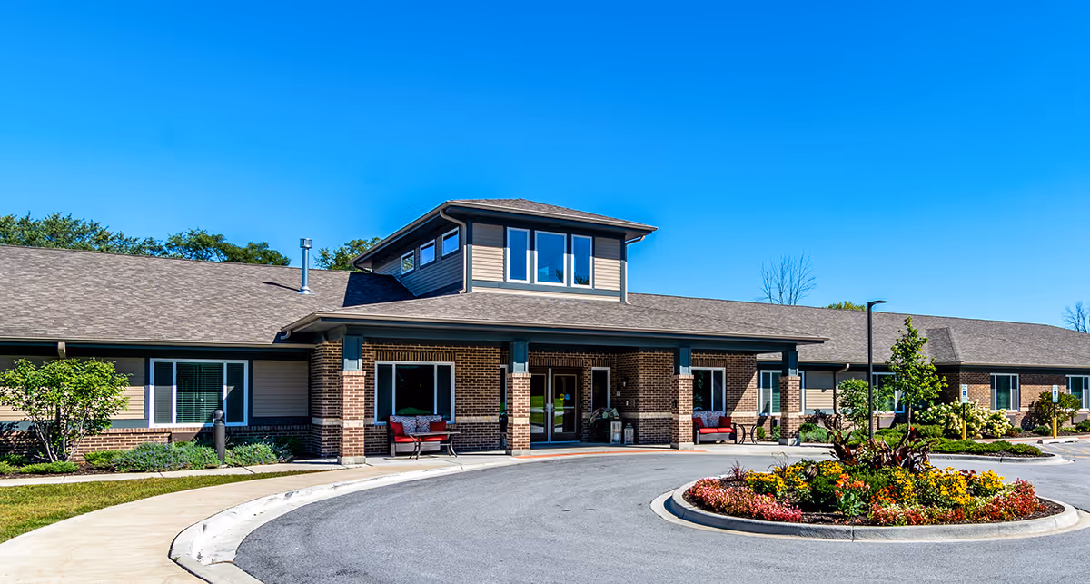 Exterior view of Porter Place, a single-story brick building with a covered entrance, large windows, and a circular driveway with a landscaped flower bed in front. The sky is clear and blue.