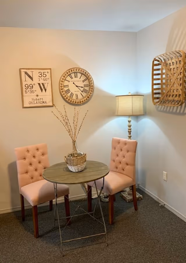 Small interior seating area with a round table, two tufted pink chairs, a floor lamp, wall clock and decorative accents.