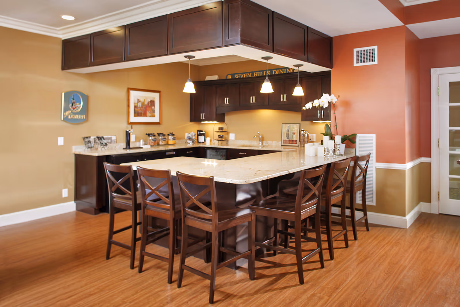 Bright communal dining area with a large marble-topped island and wooden bar stools beneath pendant lights.