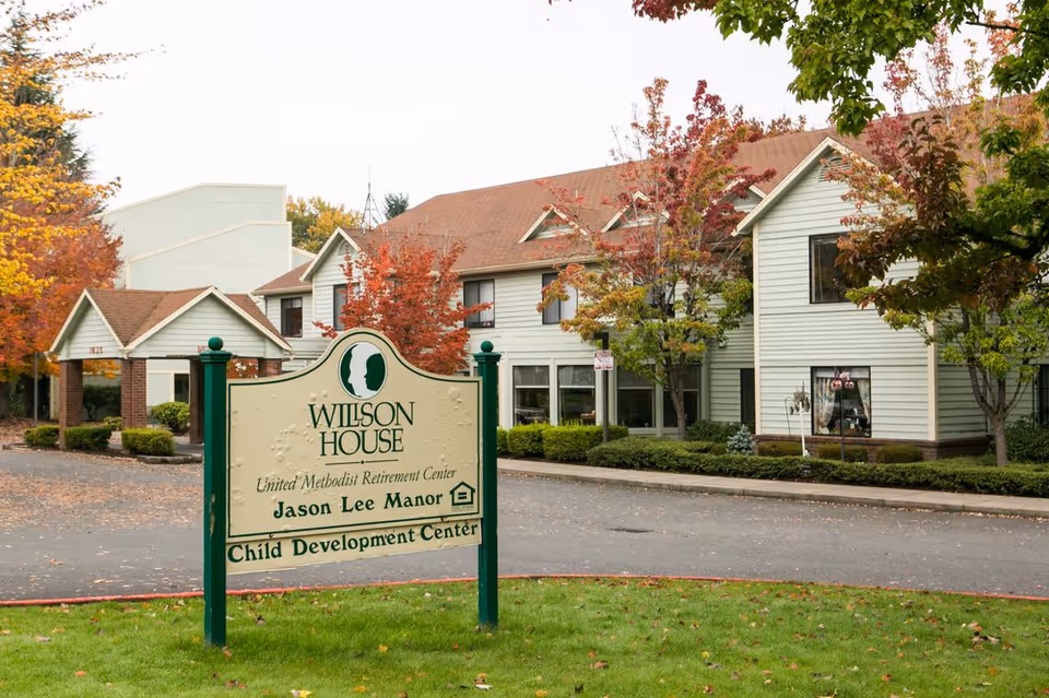 Exterior view of Willson House senior living facility with a sign and autumn trees.