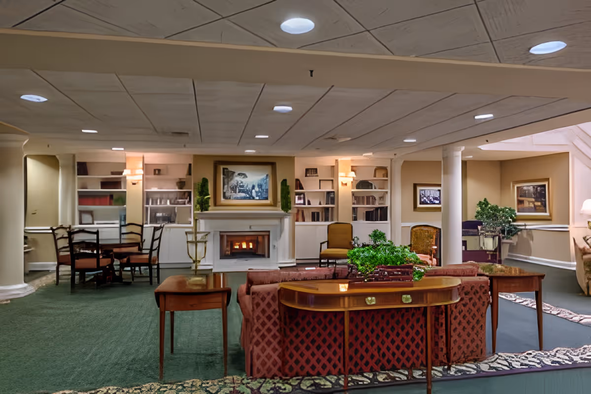 Spacious carpeted common room with sofas, chairs, tables, bookshelves, and a fireplace.