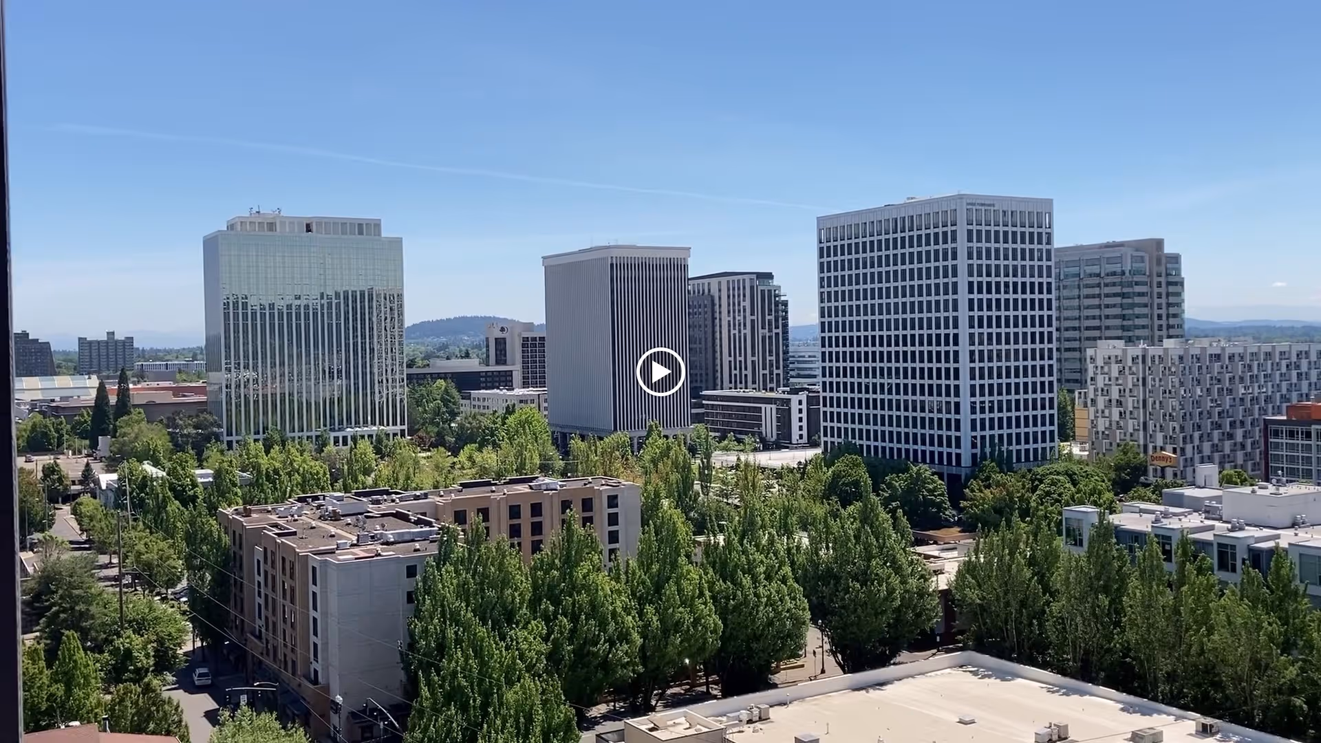 View of a cityscape with several mid-rise office buildings surrounded by many green trees under a clear blue sky.