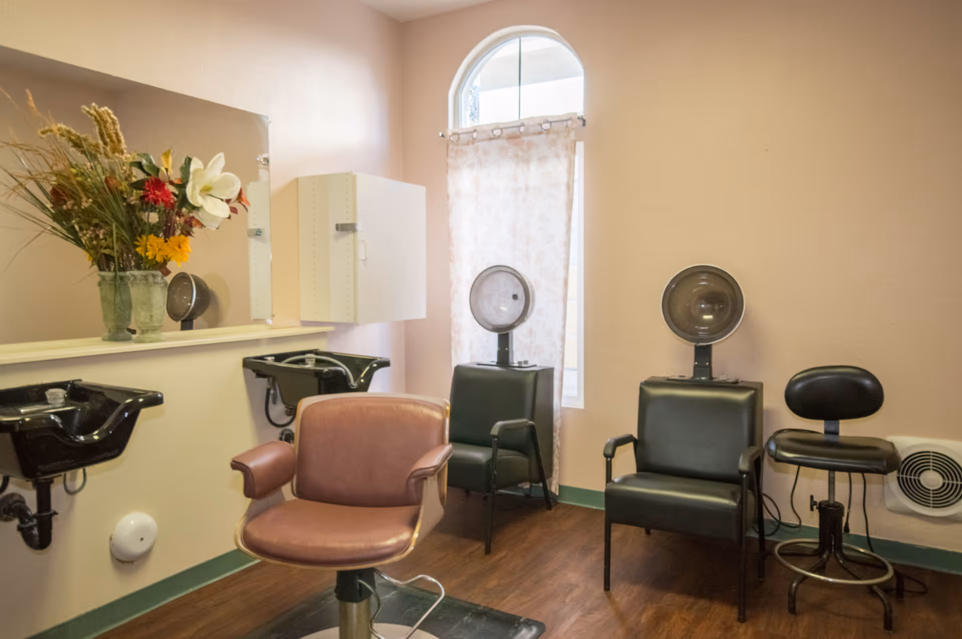 Small salon in an assisted living facility with styling chairs, wash basins, and hooded hair dryers.