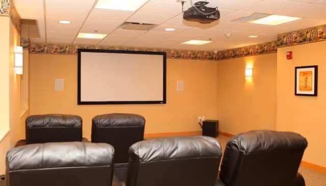 Small screening room with leather recliners facing a wall-mounted projection screen and ceiling projector.