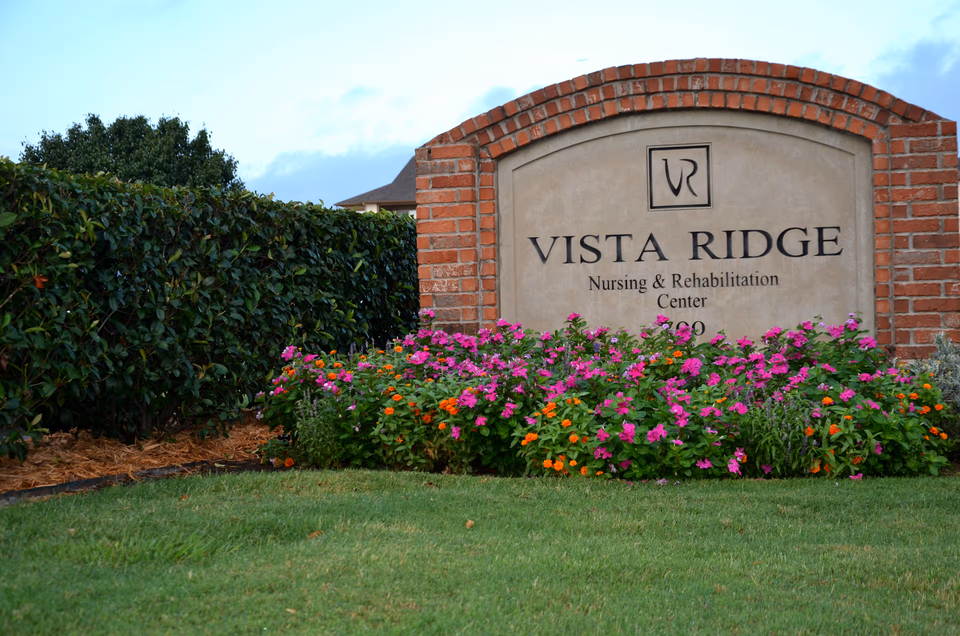 A brick and stone sign for Vista Ridge Nursing & Rehabilitation Center surrounded by colorful flowers and green bushes with a grassy lawn in the foreground.