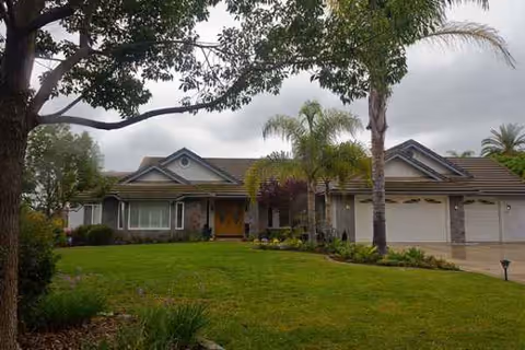 Single-story assisted living facility front exterior with lawn, trees, and a two-car garage.