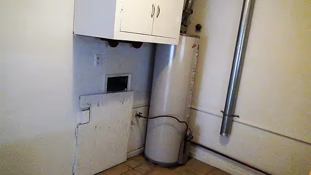 Small utility room with a tall water heater, vent pipe, wall cabinet and a laundry hookup.