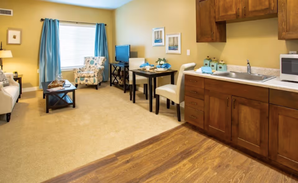 Studio living area with a small kitchen, dining table, sofa, accent chair, and TV.