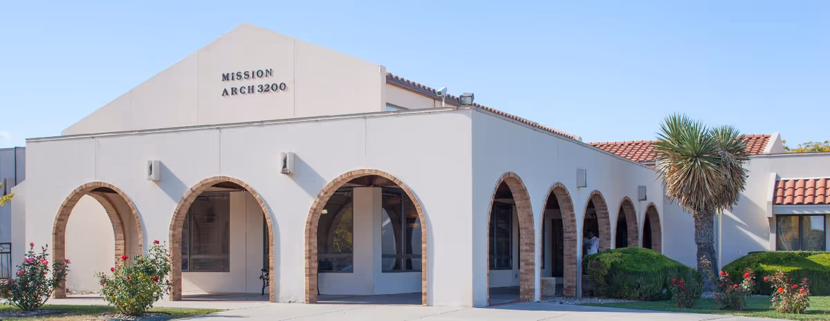 Front exterior of the Mission Arch 3200 building featuring arched walkways, stucco walls, a tiled roof, and landscaping including a palm tree.