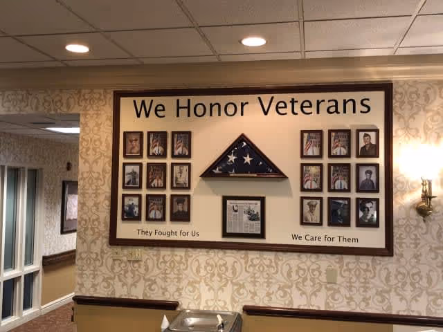 Interior hallway wall display honoring veterans with a framed folded flag, multiple portrait photos, and the words "We Honor Veterans."