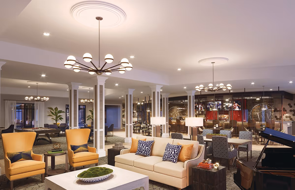 A spacious and well-lit senior living facility common area featuring comfortable seating with beige sofas and orange armchairs, a coffee table with decorative greenery, multiple dining tables with patterned chairs, a grand piano, and a bar area with multiple TV screens. The room has modern chandeliers, white columns, and large windows with curtains.
