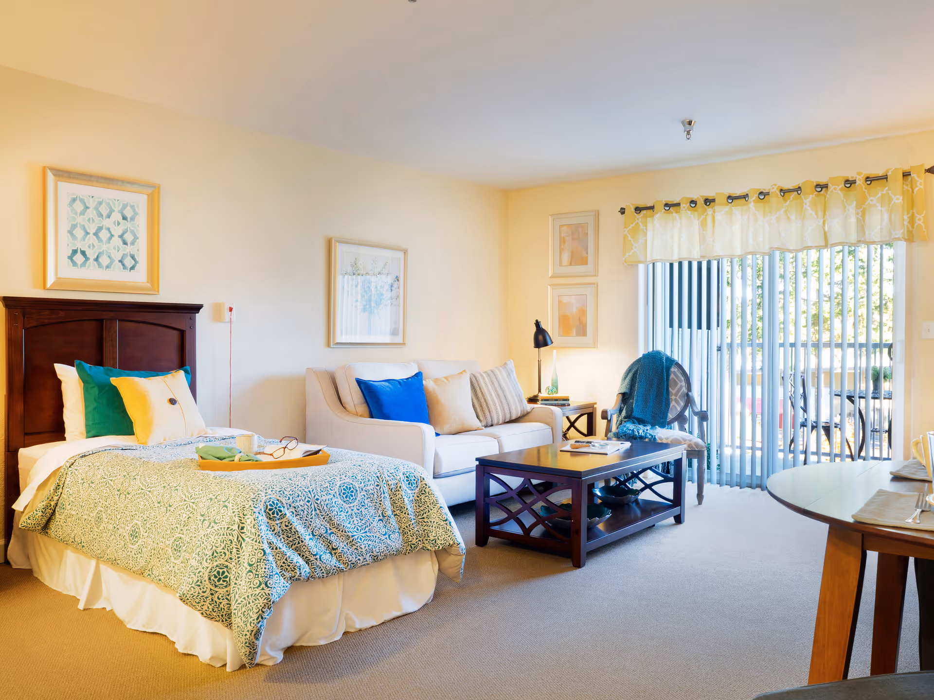 A bright studio apartment-style room with a bed, sofa, coffee table and sliding glass doors to a balcony.