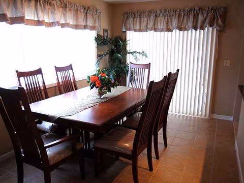 A wooden dining table with chairs and a flower centerpiece in a bright dining room.