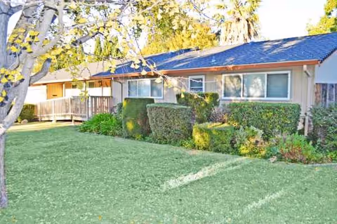 Front exterior of a single-story senior residence with green lawn and hedges.