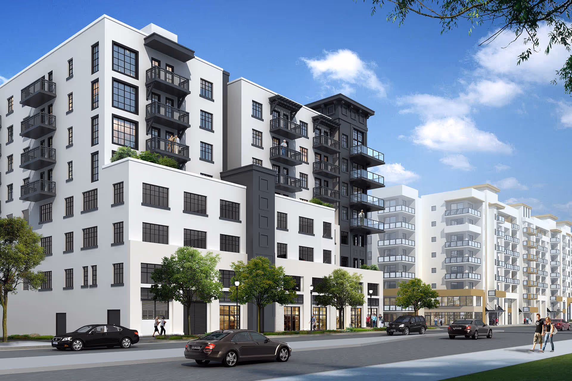 Modern multi-story residential building with white and dark gray exterior, featuring balconies, large windows, trees along the sidewalk, and cars parked on the street under a partly cloudy blue sky.