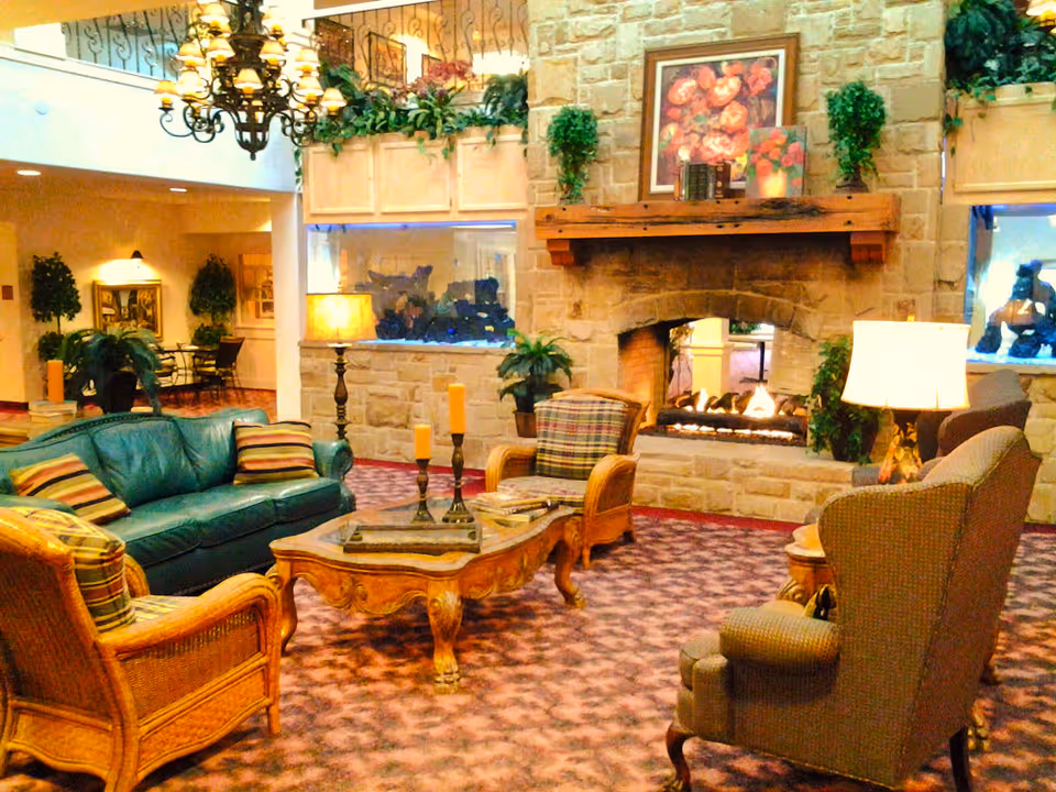 Cozy lounge area with upholstered sofas and armchairs arranged around a coffee table in front of a stone fireplace.