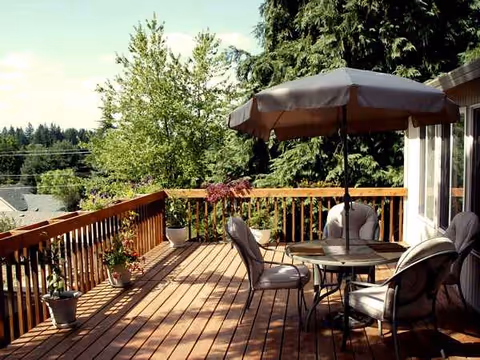 An outdoor wooden deck with a round table, chairs, umbrella, and potted plants.