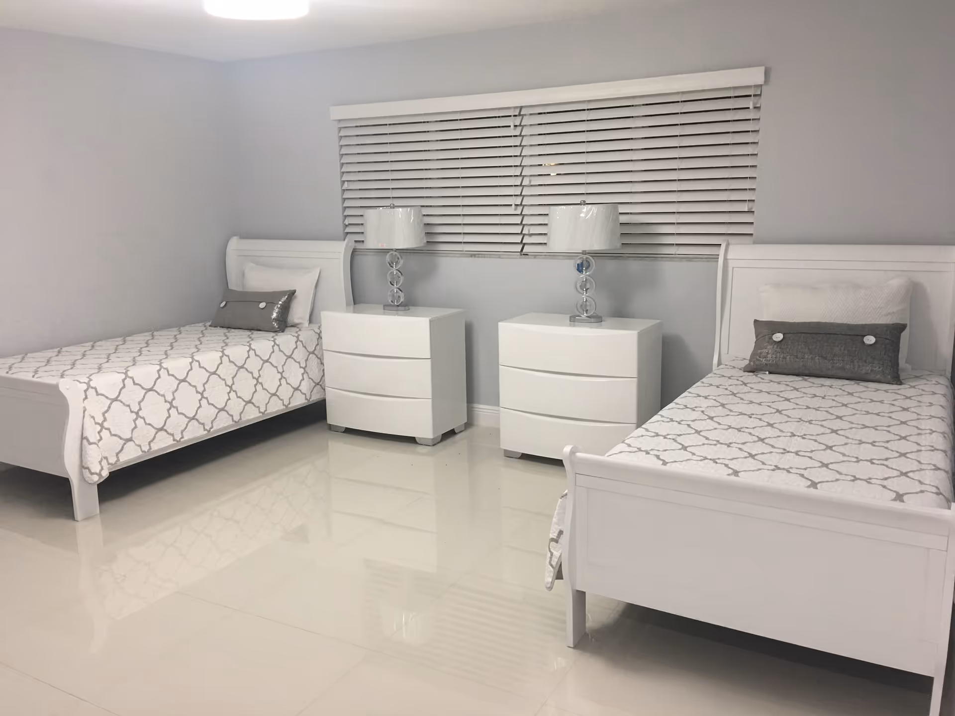 A brightly lit bedroom featuring two single beds with white frames and patterned bedding.