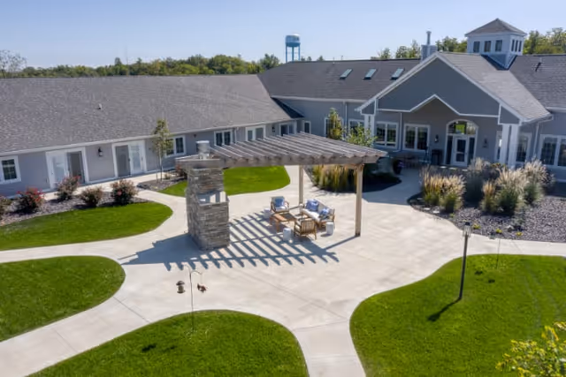 Aerial view of a senior living courtyard with a pergola-shaded seating area, paved walkways, lawns, and the surrounding single-story building.