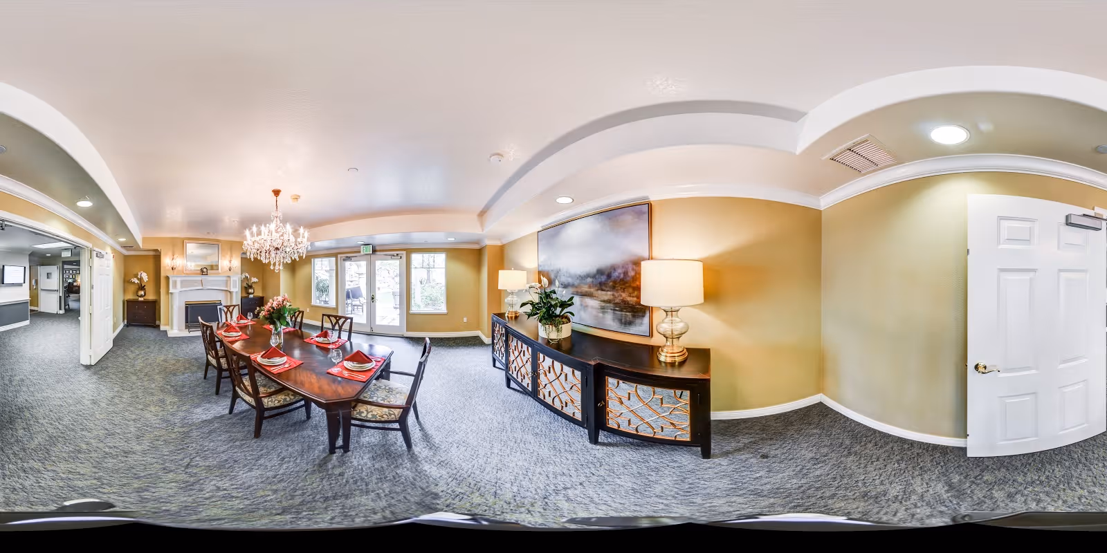 Dining room with a long wooden table set with red napkins, a chandelier overhead, buffet table, and fireplace in a common interior area.