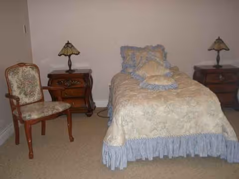 A bedroom with a single bed, two nightstands, lamps, and an upholstered chair.