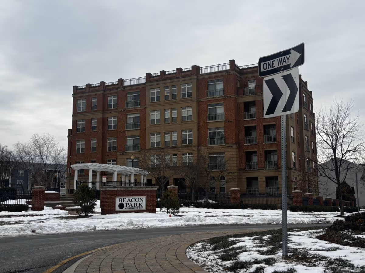 Exterior front view of a multi-story brick residential building with a 'Beacon Park' sign, a one-way street sign, and snow on the ground.