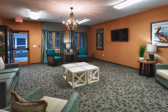 Senior living lounge with teal seating, coffee table, and orange walls.