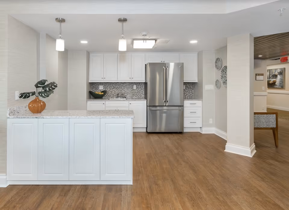Modern kitchenette with white cabinetry, a marble-topped island, and a stainless steel refrigerator in a communal living space.
